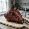 Whole bone-in smoked ham baked with a dark brown sugar glaze on a wooden carving board, shank bone showing