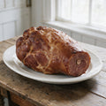 Skinless and shankless bone-in smoked ham on a white platter, trimmed lean with the flat sawn shank end showing the bone